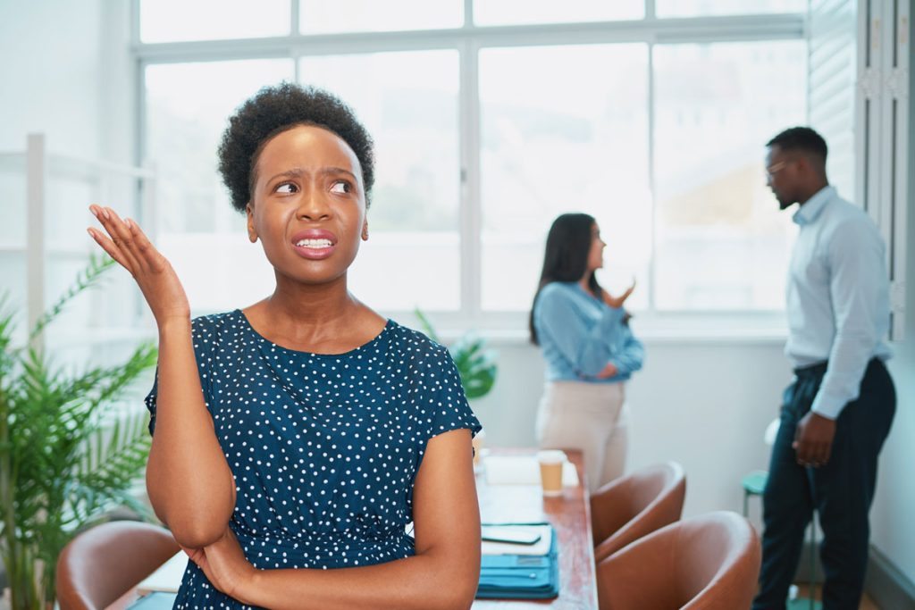 Young Black Woman Looks Upset While Colleagues Talk Behind Her Back Office Drama